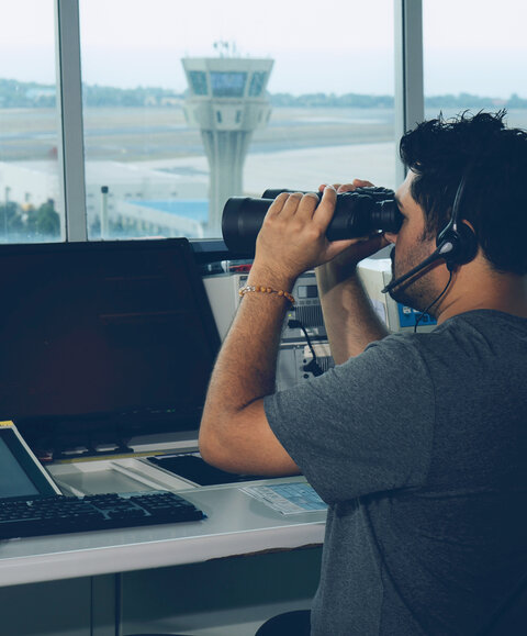 Man using binoculars to look over airport from tower
