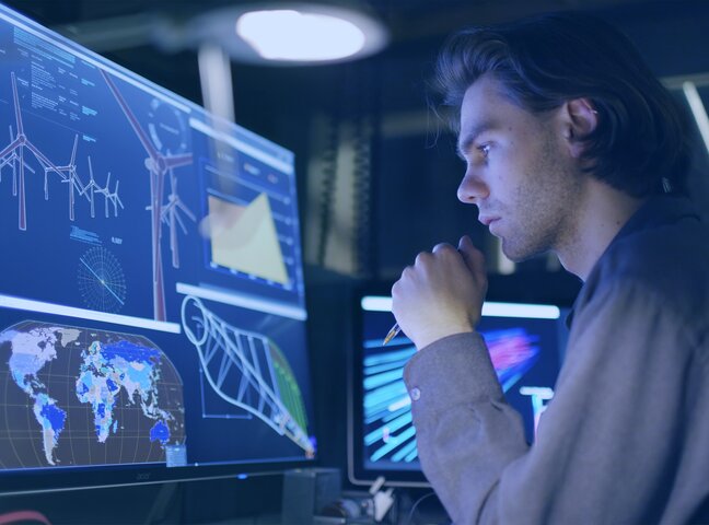 Mann sitzt vor einem Monitor und arbeitet an verschiedenen in Fenstern angeordneten Quellen. 